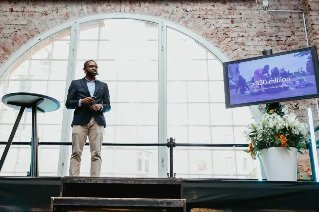 A founder presenting on stage beside a slide reading: more than 850 million Africans living under $5.50 a day